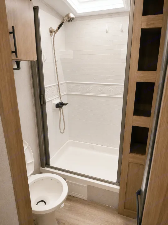 RV rental bathroom features a compact, tiled shower with a handheld showerhead, toilet, and modern wood cabinetry.. Grand Design Imagine 2024