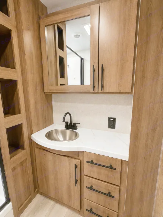 Modern RV rental bathroom vanity with wood-look cabinets, a stainless steel sink, black faucet, and practical storage shelves.. Grand Design Imagine 2024