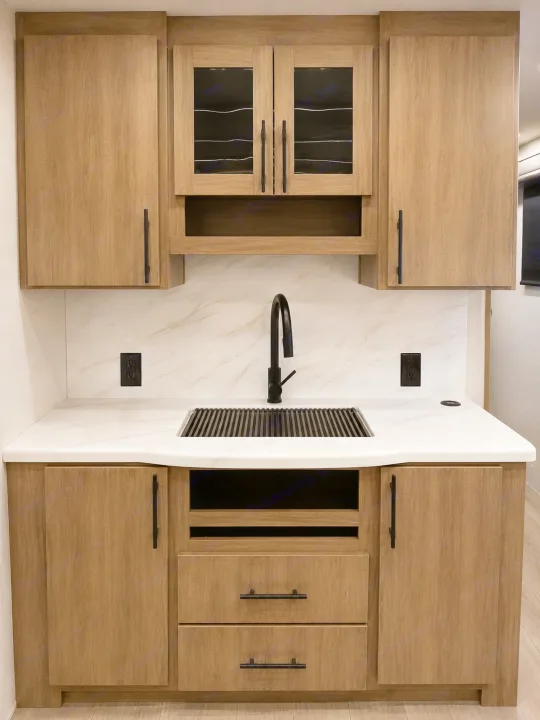 This RV rental features a modern kitchen with light wood-grain cabinetry, a white marble-look countertop, and a sleek black sink.. Grand Design Imagine 2024