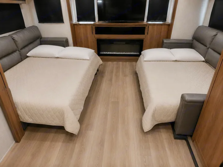 RV rental: Cozy interior with two beds, white pillows, quilted covers, wood flooring & a fireplace. Ideal for travel.. Grand Design Imagine 2024