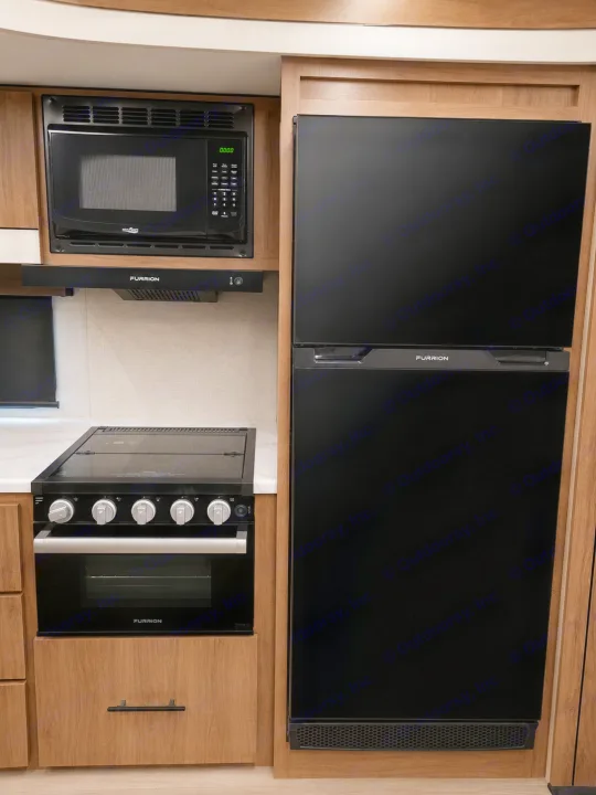 Compact RV rental kitchen featuring black Furrion appliances: microwave, range hood, stove with oven, and a large refrigerator.. Grand Design Imagine 2024