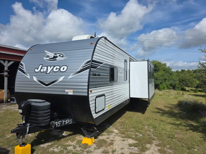 Gray Jayco travel trailer RV rental, parked on grass with its slide-out extended. Ideal for your next outdoor adventure.. JAYCO JAY FLIGHT SLX 2026