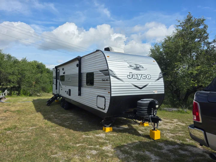A modern Jayco travel trailer RV rental sits on a grassy site with stabilization blocks under a bright, cloudy sky.. JAYCO JAY FLIGHT SLX 2026