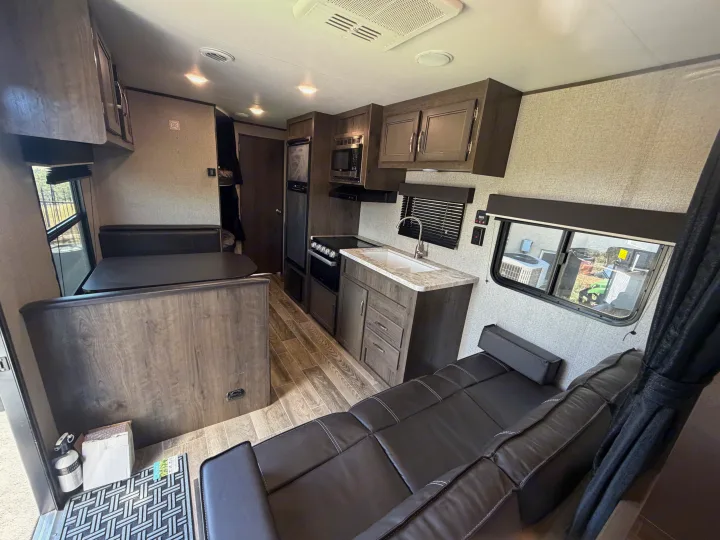 Modern RV rental interior. Features a compact kitchen (sink, stovetop, microwave), dining booth, and sofa, ideal for travel.. Jayco Jay Flight SLX 2021