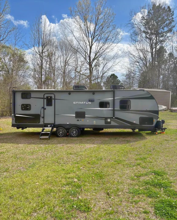 Explore with this grey Stratus travel trailer RV rental, parked on a grassy field with trees. Perfect for your next adventure!. Venture Venture Trailer 2023