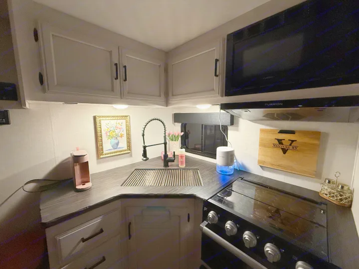 Bright RV rental kitchen view: corner sink, stove, microwave, coffee maker, and charming decor. Your home on wheels.. Venture Venture Trailer 2023