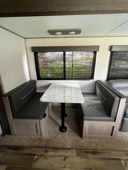Cozy rv rental dinette featuring dark booth seating, a sleek marble-look table, and windows with blinds.. Dutchmen Coleman Lantern LT 2022