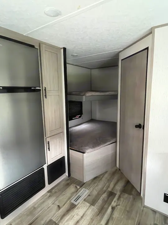 Inside a modern RV rental: bunk beds, a stainless steel refrigerator, and wood-look flooring, ideal for family travel.. Dutchmen Coleman Lantern LT 2022
