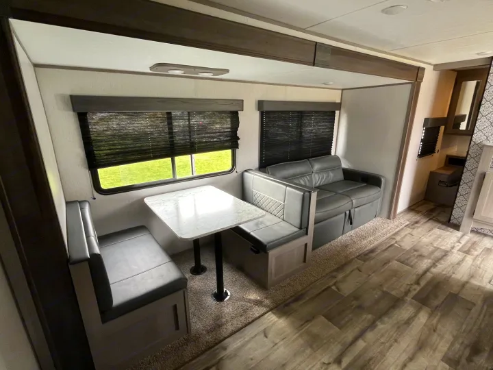 Modern gray dinette and sofa in an rv rental living area, with large windows, blinds, and mixed flooring.. Dutchmen Coleman Lantern LT 2022