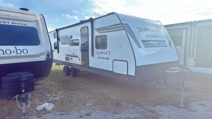 RV rental options: A white Sunset Trail Sport travel trailer and a tan Nobo RV are parked outdoors under a blue sky.. Crossroads RV Sunset Trail Sport 2025