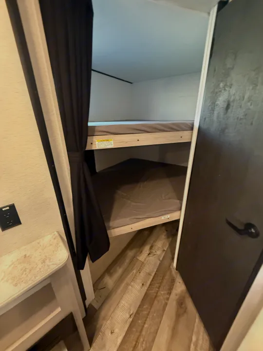 Cozy bunk beds in an **rv rental**, featuring dark privacy curtains and wood-look flooring. Ideal for family adventures.. Crossroads RV Sunset Trail Sport 2025