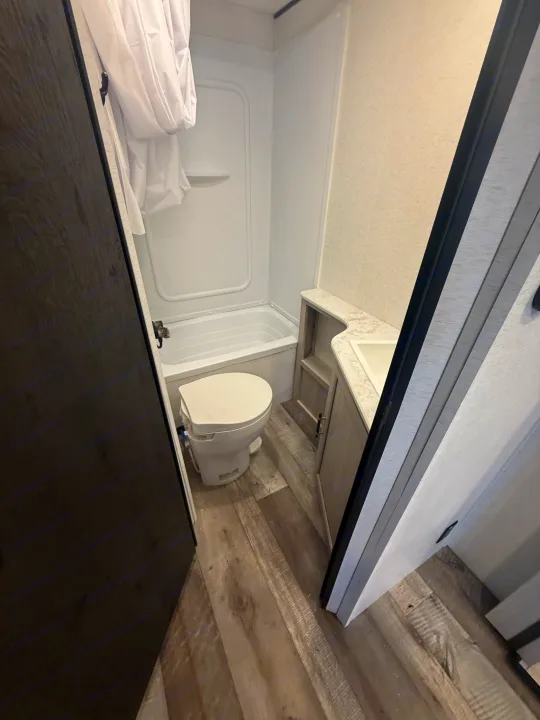 This clean RV rental bathroom features a compact toilet, small tub/shower combo, and sink vanity, designed for travel convenience.. Crossroads RV Sunset Trail Sport 2025