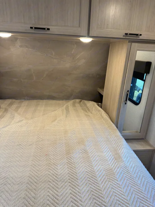 RV rental bedroom with light wood grain cabinets, under-cabinet lighting, marbled headboard, and a chevron-patterned bed.. Crossroads RV Sunset Trail Sport 2025