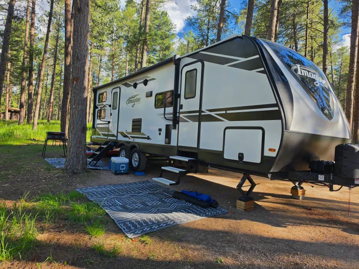 Enjoying nature with an RV rental! A travel trailer set up in a pine forest campsite, complete with outdoor living essentials.. Grand Design Imagine 2022