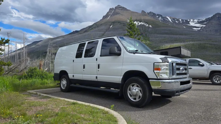 White Ford E-Series RV rental van parked in a mountain landscape with fire-damaged trees under a cloudy sky.. Ford Econoline 2011