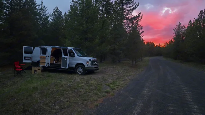Experience van life camping with an rv rental! This camper van is perfectly parked by a forest road under a vibrant sunset.. Ford Econoline 2011