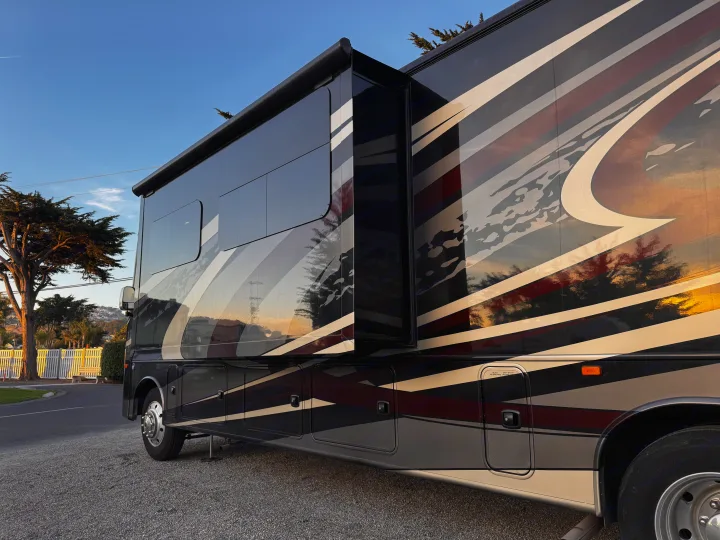Experience comfort in this luxurious dark RV rental at sunset, featuring reflective stripes, an extended slide-out, and a deployed awning.. Jayco Precept 2019