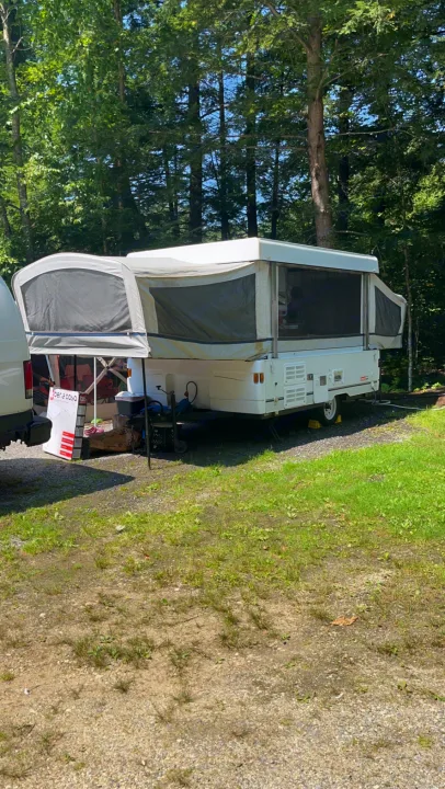 Pop-up RV rental camper set up under sun-dappled trees at a peaceful campsite, ready for outdoor living and travel.. Coleman Santa Fe 2003