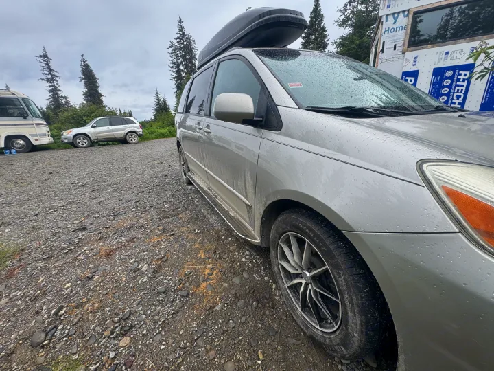 Wet minivan with roof cargo box, RV rental, and SUV on a gravel road next to a building wrapped in Henry R-TECH.. Toyota Toyota Sienna XLE 2005