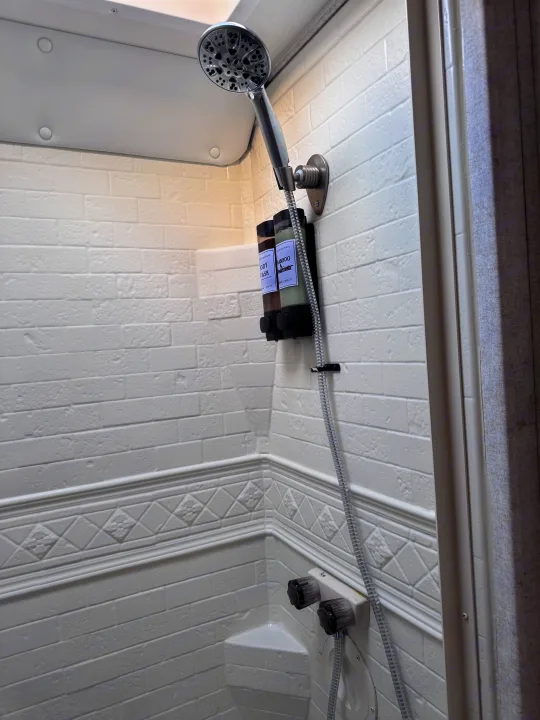 Clean RV rental shower with a handheld shower head, wall-mounted soap dispensers for body wash/shampoo, and white textured walls.. Forest River Sunseeker LE 2018