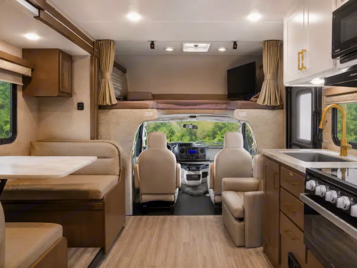 Bright rv rental interior from rear, showing dinette, kitchen with golden faucet, front cabin, and an overhead bunk.. Thor Four Winds 2024