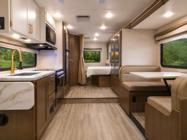 Spacious rv rental interior featuring a modern kitchen, comfortable dinette, and bed area, with light wood floors and nature views.. Thor Four Winds 2024