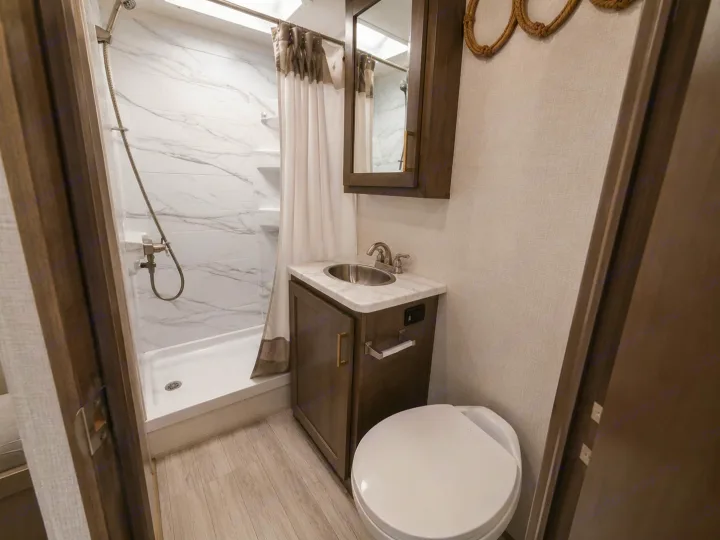 This RV rental bathroom features a compact shower with marble-look tiles, a vanity with sink, and a toilet. Maximizing space for travelers.. Thor Four Winds 2024