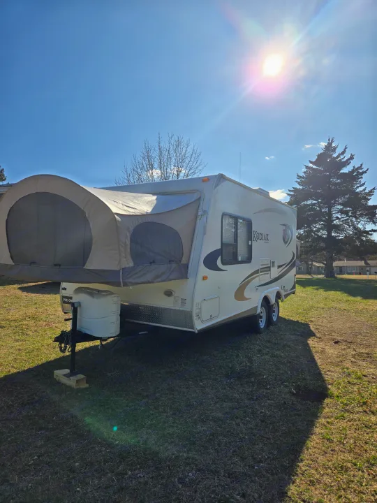 Kodiak hybrid travel trailer (pop-out tent) for RV rental, parked on grass under a sunny sky.. Dutchmen Kodiak 2010