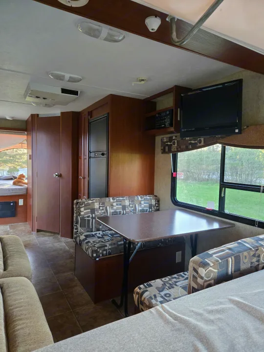 An inviting rv rental interior: dinette, kitchen, TV, and a peek into a bedroom with a cat. Comfortable camper space.. Dutchmen Kodiak 2010