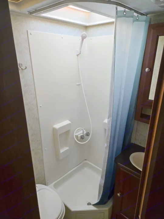 Compact RV rental bathroom with a shower, toilet, and dark wood vanity with a sink. Features a blue shower curtain and skylight.. Dutchmen Kodiak 2010