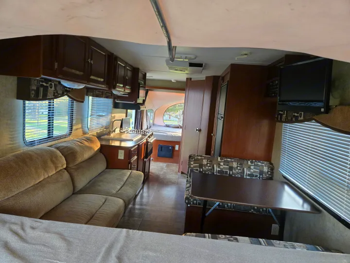Interior of an RV rental, featuring a kitchen, comfortable sofa, dining area, and a pop-out bed at the rear.. Dutchmen Kodiak 2010