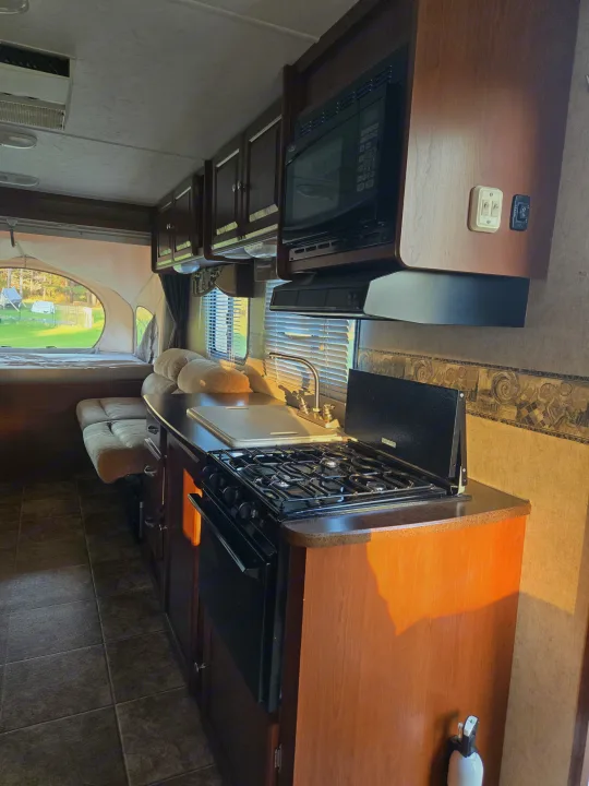 RV rental interior featuring a kitchenette with stovetop, sink, microwave, and a pop-out bed in the background.. Dutchmen Kodiak 2010
