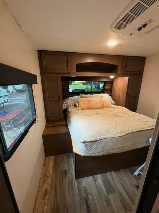 Cozy RV rental bedroom featuring a comfy bed, wooden cabinets, window views, and a ceiling AC unit.. Venture Venture Trailer 2023
