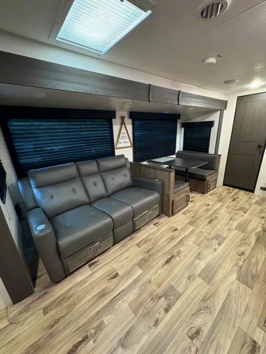 Spacious RV rental interior with a gray reclining sofa, dinette, skylight, and wood-look floor, ideal for comfort.. Venture Venture Trailer 2023