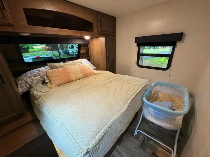 Cozy RV rental bedroom featuring a large bed, overhead storage, and a baby bassinet on the right, great for family stays.. Venture Venture Trailer 2023