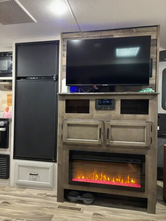 This RV rental interior showcases a modern entertainment center with a TV, electric fireplace, and a full-size refrigerator.. Venture Venture Trailer 2023