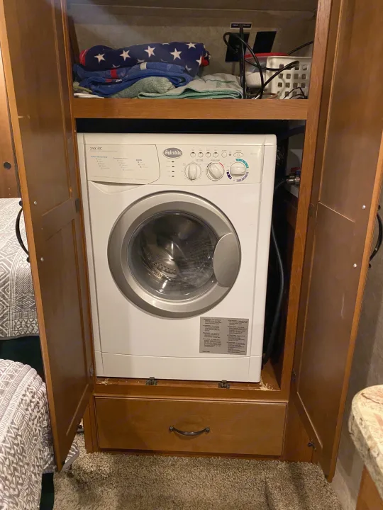 A white Splendide compact washer/dryer combo integrated into a wooden cabinet in an RV, perfect for rv rental trips.. Keystone RV Montana High Country 2013