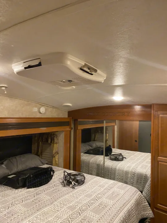 RV rental bedroom: a bed with patterned quilt, overhead AC unit, and mirrored closet. Ready for comfortable travel.. Keystone RV Montana High Country 2013