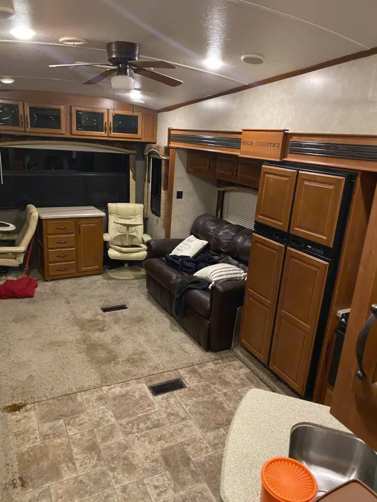 Comfortable rv rental interior showing a living area with sofa, chairs, kitchen, and wood cabinetry. Ideal for travel.. Keystone RV Montana High Country 2013