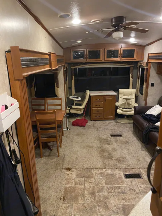 RV rental interior: dining area, sofa, and bunk beds, showing visibly stained carpet and tiled flooring.. Keystone RV Montana High Country 2013