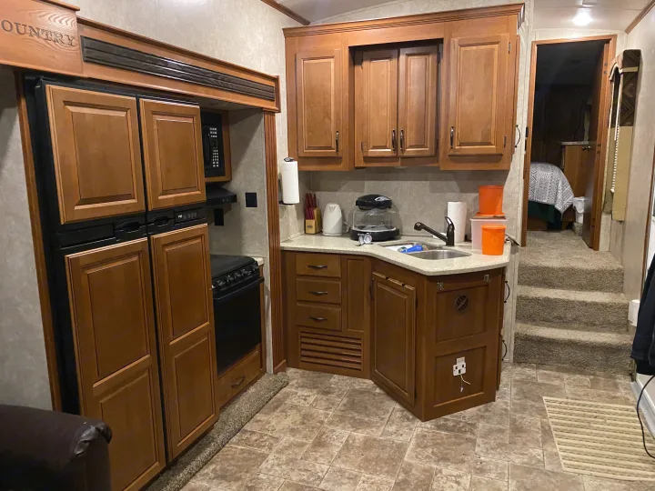 Spacious RV rental kitchen featuring wood cabinets, fridge, stove, microwave, and sink, with steps to the bedroom.. Keystone RV Montana High Country 2013