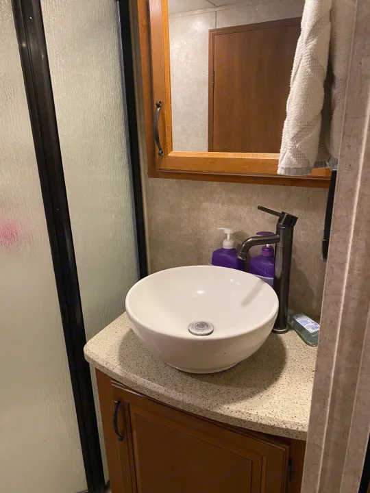 RV rental bathroom featuring a vessel sink, dark faucet, wooden vanity, and textured shower door.. Keystone RV Montana High Country 2013