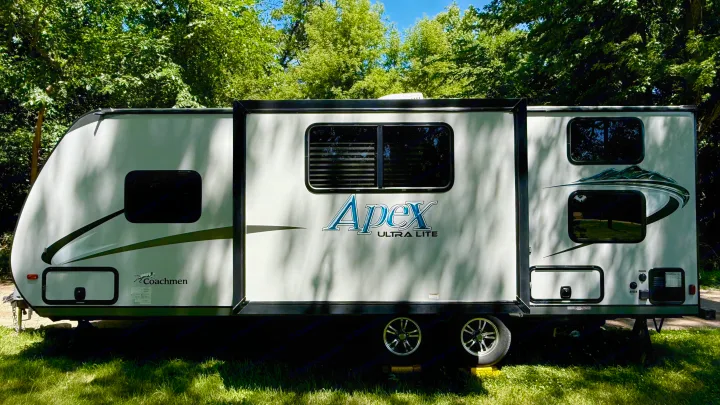 This Coachmen Apex Ultra Lite travel trailer RV rental is set up for outdoor camping in a lush, green setting.. Coachmen Apex 2016