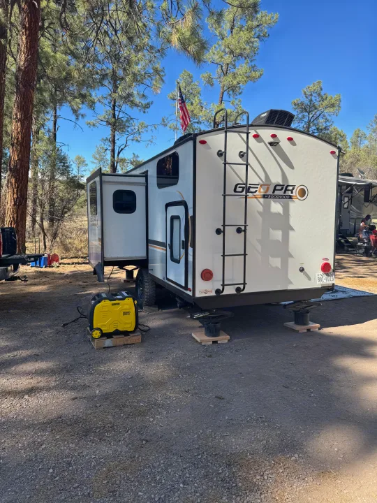 Geo Pro RV rental parked at a serene campsite with a generator, stabilizers, and an American flag among tall pine trees.. Forest River Rockwood Geo Pro 2022