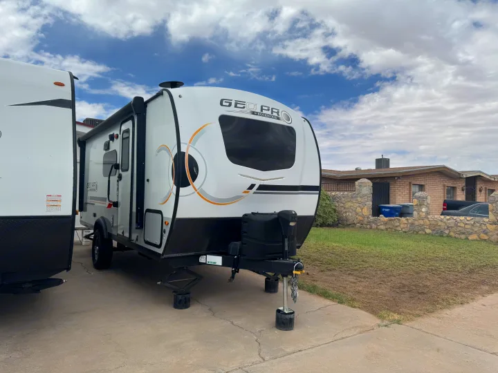 A white & grey Geo Pro travel trailer, a ready RV rental, parked on a driveway with stabilization jacks. Houses & a cloudy sky in background.. Forest River Rockwood Geo Pro 2022