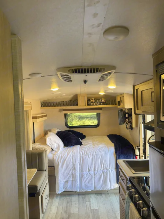 This RV rental showcases a compact interior with a bed, small kitchen with stove, and a dinette. Overhead, an AC unit and lights illuminate the space.. Forest River Rockwood Geo Pro 2022
