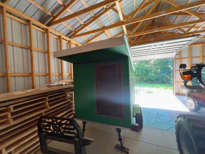 A small, green, custom-built portable cabin, potentially for rv rental, sits inside a barn with an open garage door.. Custom Custom 2025