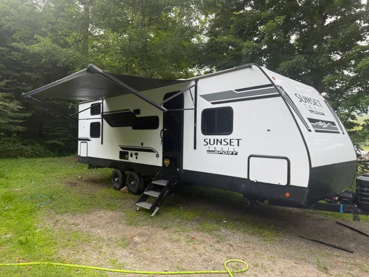 White Sunset Trail Sport rv rental with awning extended, parked on grass by trees, ready for your outdoor camping adventure.. Crossroads RV Sunset Trail Sport 2025