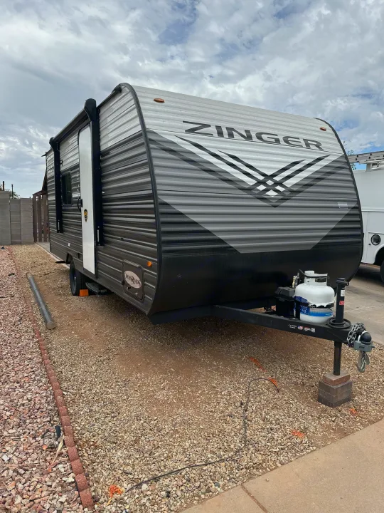 This Zinger RV rental, a gray and black travel trailer, is parked on a gravel lot under cloudy skies, ready for a trip.. Crossroads RV Zinger Lite 2026