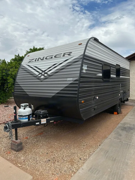 Modern Zinger travel trailer RV rental, featuring a grey and black striped exterior, parked on gravel under a cloudy sky.. Crossroads RV Zinger Lite 2026